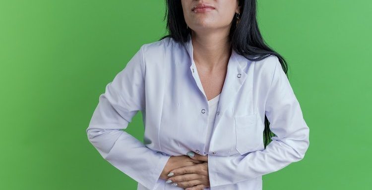 aching young female doctor wearing medical robe holding belly with closed eyes isolated on green background with copy space
