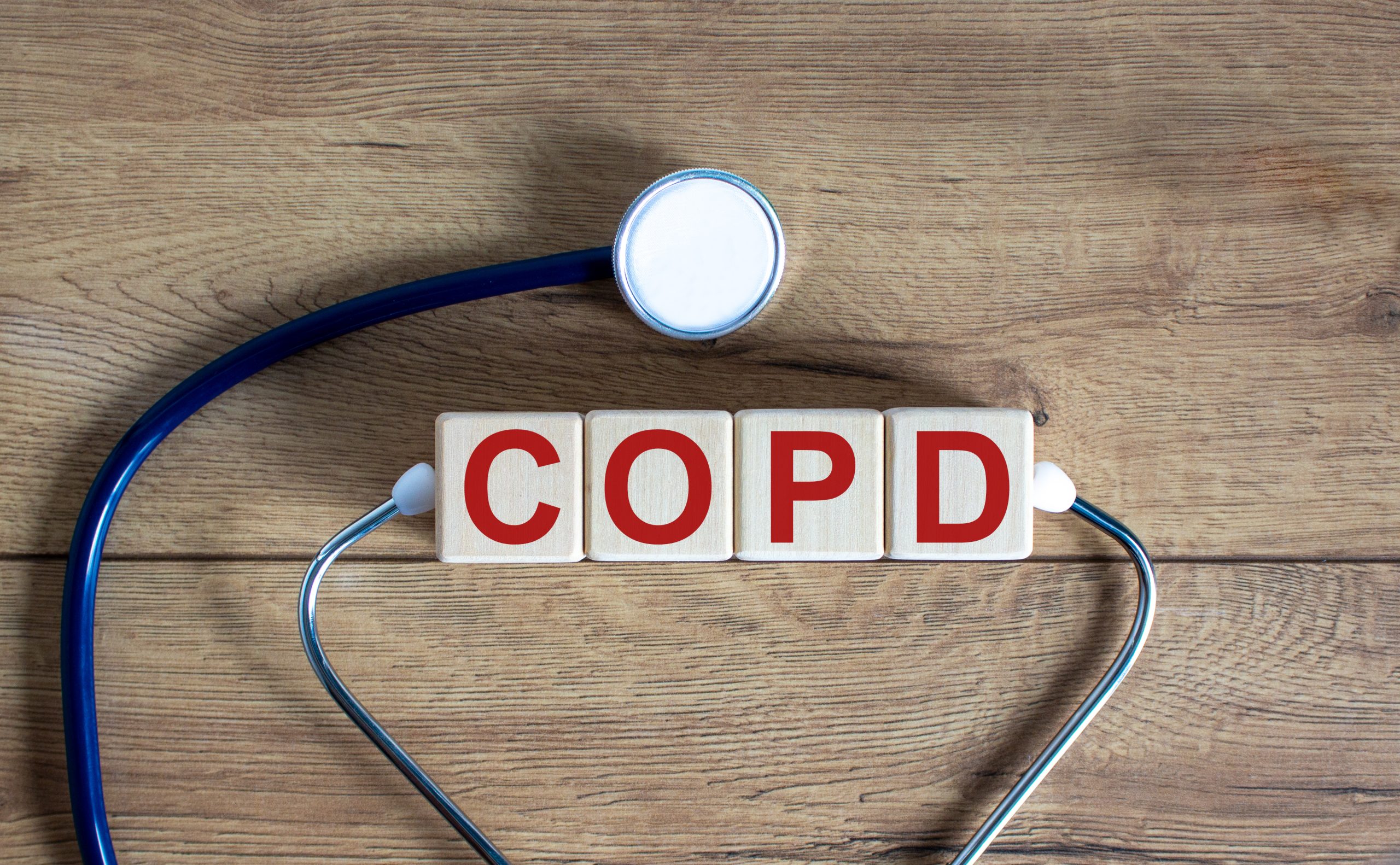 COPD medical concept. Wooden cubes with the inscription 'COPD - chronic obstructive pulmonary disease', stethoscope. Beautiful wooden background. Copy space.