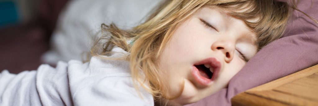 funny face expression with open mouth of blonde caucasian three years old child, sleeping on king bed snoring