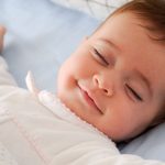 Smiling baby girl lying on a bed sleeping and smiling on blue sheets, infant, safe sleep