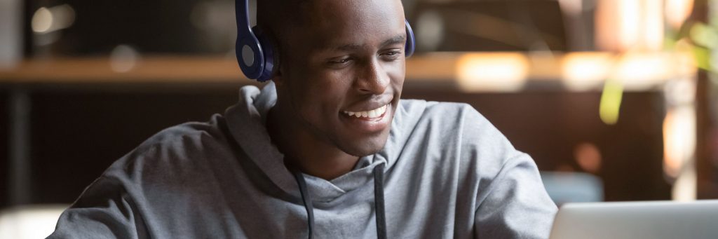 Smiling african young man student wear headphones looking at laptop screen writing notes, happy black guy e-learning in internet study online with skype teacher on computer watch webinar