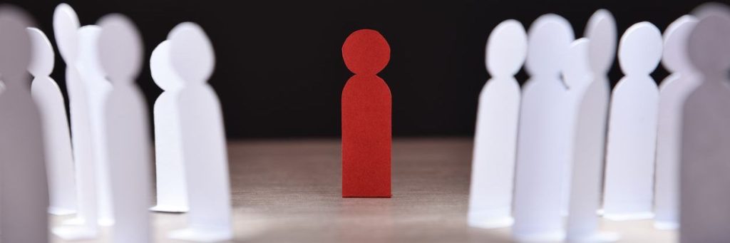 religious discrimination, social discrimination concept with many little white paper men around a different one on wooden base and dark background