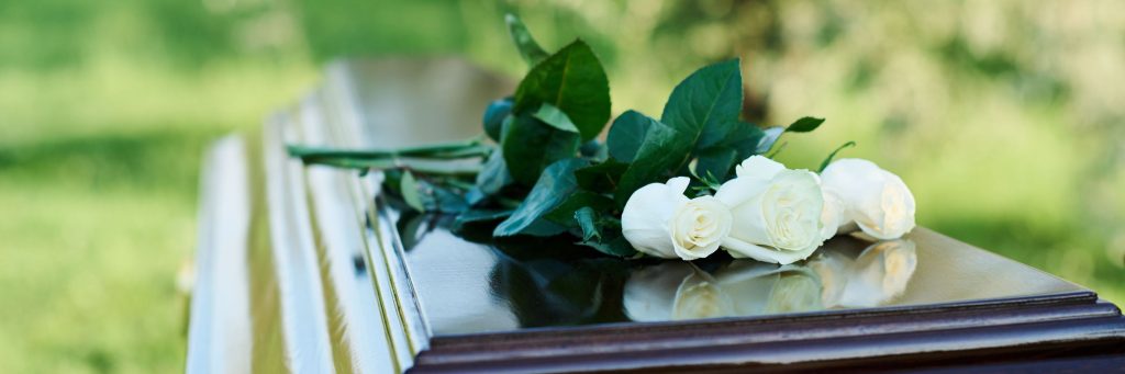 maternal mortality, Focus on bunch of several fresh white roses lying on top of closed lid of wooden coffin standing in front of camera at modern graveyard