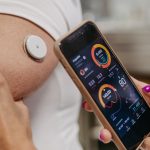 Doctor connecting continuous glucose monitor with smartphone, to check blood sugar level in real time. Obese, overweight man is at risk of developing type 2 diabetes, T2D, T2DM
